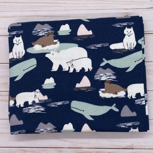 May include: Folded navy blue fabric with a repeating pattern of arctic animals. The design includes white polar bears, gray whales, brown seals, white foxes, and stylized icebergs in shades of gray and pink.