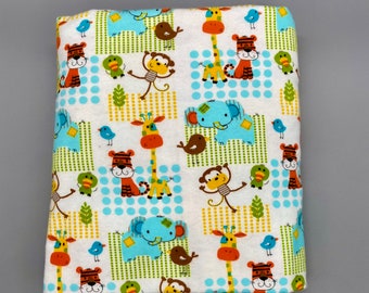 May include: White fabric featuring a repeating pattern of cartoon animals such as giraffes, tigers, elephants, monkeys, and birds. The design includes blue polka dots and green and yellow square accents. The fabric is folded.