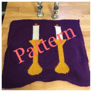 May include: A purple knitted blanket with a design of two gold candle holders with white candles and orange flames. The word "Pattern" is written across the blanket in pink.