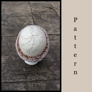 May include: A white knitted hat with a brown faux fur trim. The hat is sitting on a gray stone surface.
