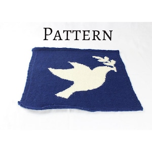 May include: A blue knitted blanket with a white dove carrying an olive branch in its beak. The blanket has the word "PATTERN" printed above the dove.