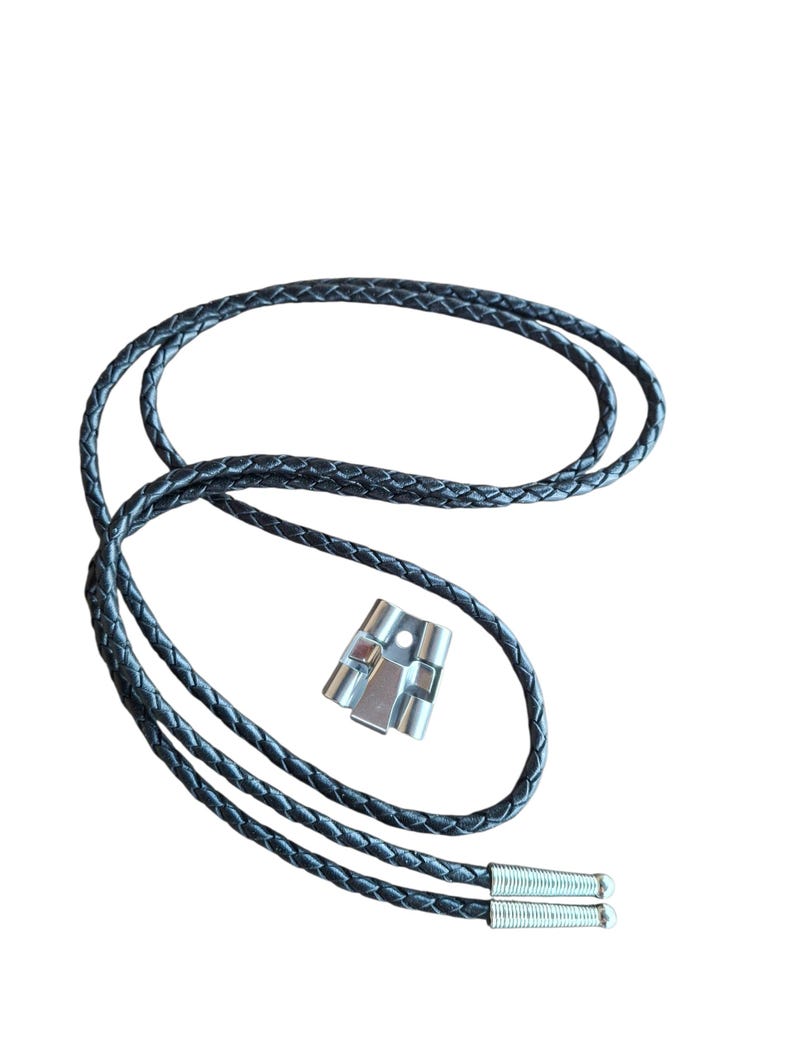 May include: A black leather bolo tie with a braided design. The tie features silver-colored metal tips and a silver-colored metal slide. The bolo tie is displayed against a white background.