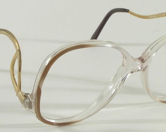 May include: Clear plastic eyeglasses with a brown rim and gold metal arms. The arms are curved and have a unique design.