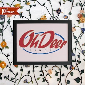 May include: A framed cross-stitch pattern of the "Oh Deer Diner" logo. The logo is red with a blue oval around it and the words "Diner" in smaller letters below.