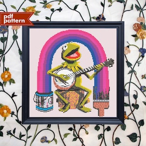 Op de afbeelding: Borduurpatroon met Kermit de Kikker die banjo speelt onder een regenboog. Het patroon bevat een verfpot en een kwast.