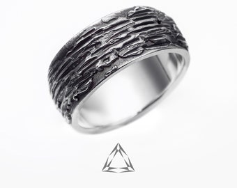 May include: A silver ring with a textured, rough surface. The ring is wide and has a unique, modern design.
