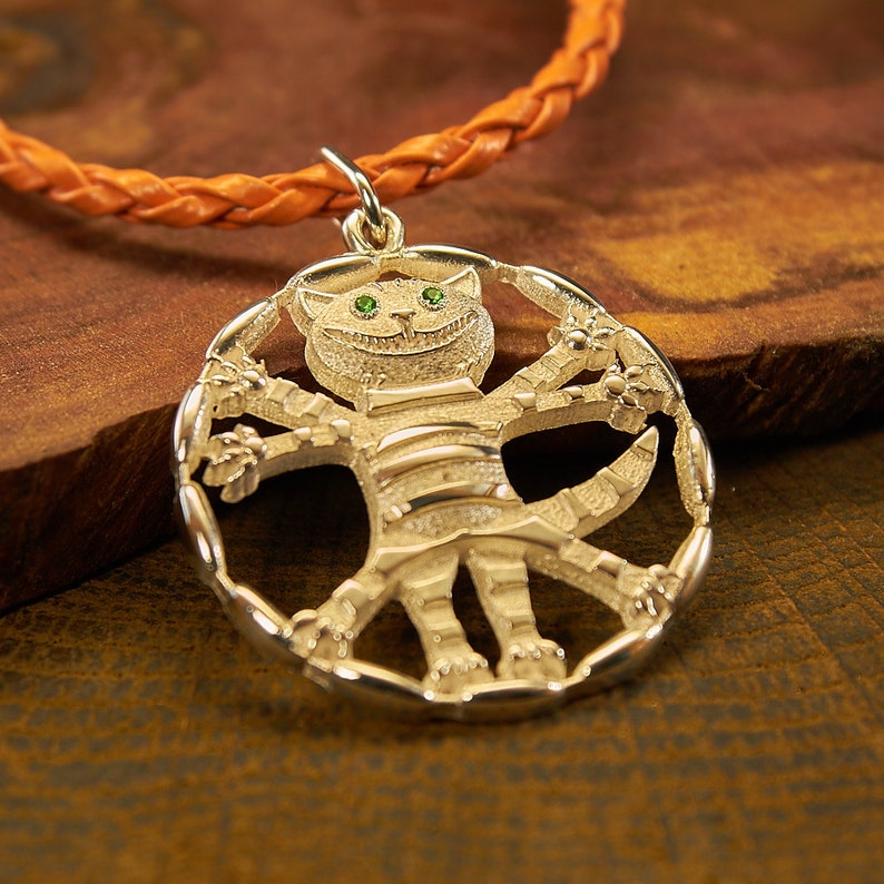Peut inclure: Un collier avec un pendentif en argent repr&eacute;sentant un chat fantaisiste aux yeux verts et au corps ray&eacute;. Le chat est repr&eacute;sent&eacute; avec les bras et les jambes tendus, formant un cercle autour du pendentif.