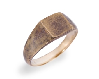 May include: A gold signet ring with a square top. The ring has a worn, distressed finish.