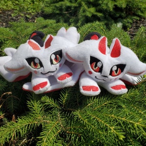 May include: Two white plush toys with red accents and black eyes. The toys are shaped like foxes with pointy ears and long tails.