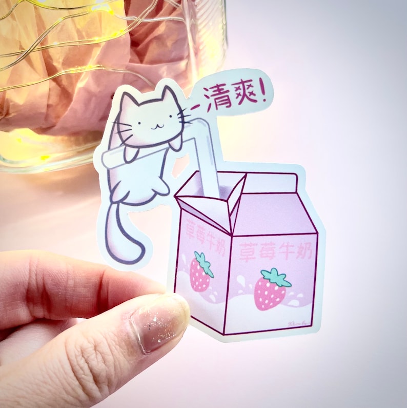 May include: A white cat with pink ears and a pink nose is drinking from a pink carton of strawberry milk. The carton has the text "草莓牛奶" on it, which is Chinese for "strawberry milk". The cat is holding a straw in its mouth and the carton is open. The cat is looking at the viewer and the text "清蒸!" is written in red on the carton.