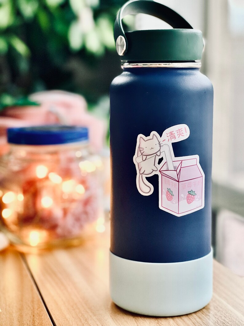 May include: A blue reusable water bottle with a white bottom and a sticker of a cartoon cat drinking from a carton of strawberry milk. The sticker says "Drink!" in Japanese.