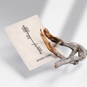 Side angle view of an Anam Cara (Soulmate) Ogham print with black Ogham script and Anam Cara text on an antique-style background, displayed beside a decorative branch.