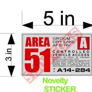 May include: A white sticker with black text that reads "Area 51" in red. The sticker also includes the text "Groom Dry Lake AFS, NV" and "Controlled Vehicle Access". The sticker is 5 inches wide and 3 inches tall.