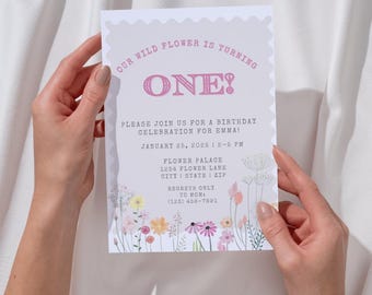 May include: A pink and white birthday invitation with a floral design. The invitation says "Our Wild Flower is Turning One!" and includes the date and time of the party, as well as the address and phone number of the host.