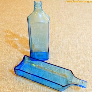 Pu&ograve; includere: Una bottiglia di vetro trasparente colorata di blu e un vassoio abbinato. La bottiglia ha una forma rettangolare con un collo stretto. Il vassoio &egrave; rettangolare con un bordo svasato. Gli oggetti sono su una superficie di colore neutro.