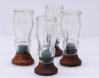 May include: Four clear glass shot glasses with a bulbous shape, set on dark wood bases. The shot glasses have a classic design, perfect for serving spirits. The bases are a rich, dark brown color.