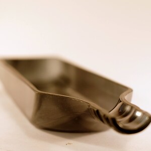 May include: A gray, plastic, elongated dish with a curved, rounded end. The dish is empty and appears to be made of a smooth, hard plastic.