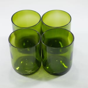 May include: Four green glass tumblers, made from recycled wine bottles, are arranged in a square formation on a white surface.