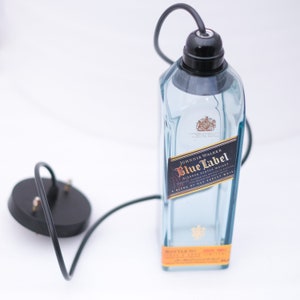 May include: A clear glass bottle with a black label that reads "Johnnie Walker Blue Label Blended Scotch Whisky A Blend of Our Rarest Whiskies". The bottle is hanging from a black cord with a black electrical socket.