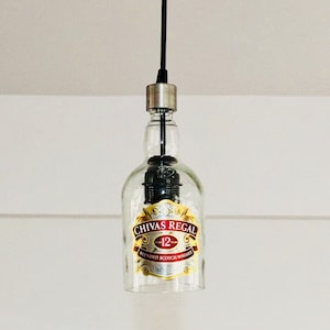Peut inclure: Une suspension en verre transparent en forme de bouteille avec un cordon noir et un bouchon argent&eacute;. La bouteille porte une &eacute;tiquette indiquant "Chivas Regal 12 ans Blended Scotch Whisky".