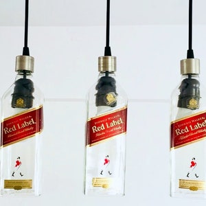 May include: Three clear glass bottles with black metal caps and black cords hanging from the ceiling. Each bottle has a red label with the text "JOHNNIE WALKER Red Label" and a small image of a man in a kilt.