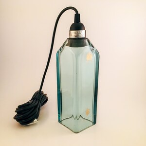 May include: A clear glass pendant light fitting with a black cord and a black metal cap. The glass is textured and has a light blue tint. The cap has the text "DO NOT EXCEED THE MAX. WATTAGE OF THE LAMP. CAUTION: REPLACEABLE BULB ONLY. MAX. WATTAGE 60W."