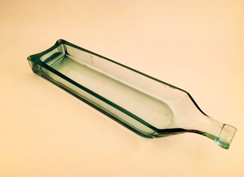 May include: A clear glass bottle that has been cut and repurposed into a serving dish. The bottle is rectangular in shape and has a rounded lip.