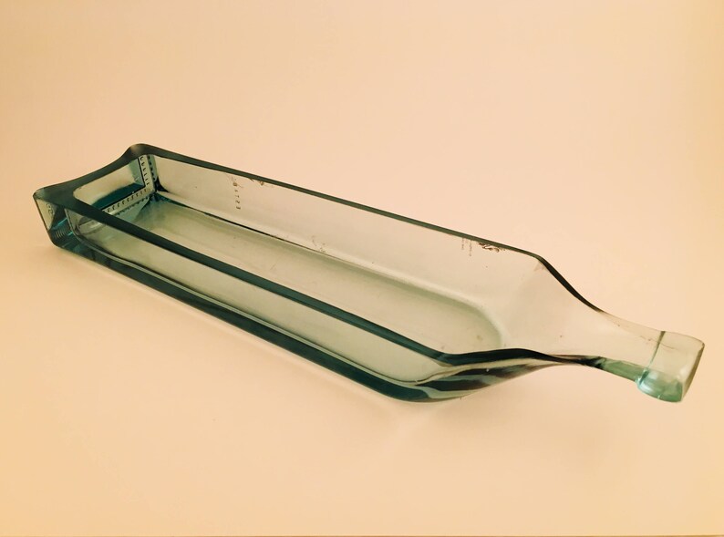 May include: A clear glass serving dish made from a recycled wine bottle. The dish is rectangular with a rounded edge and a long, narrow spout.