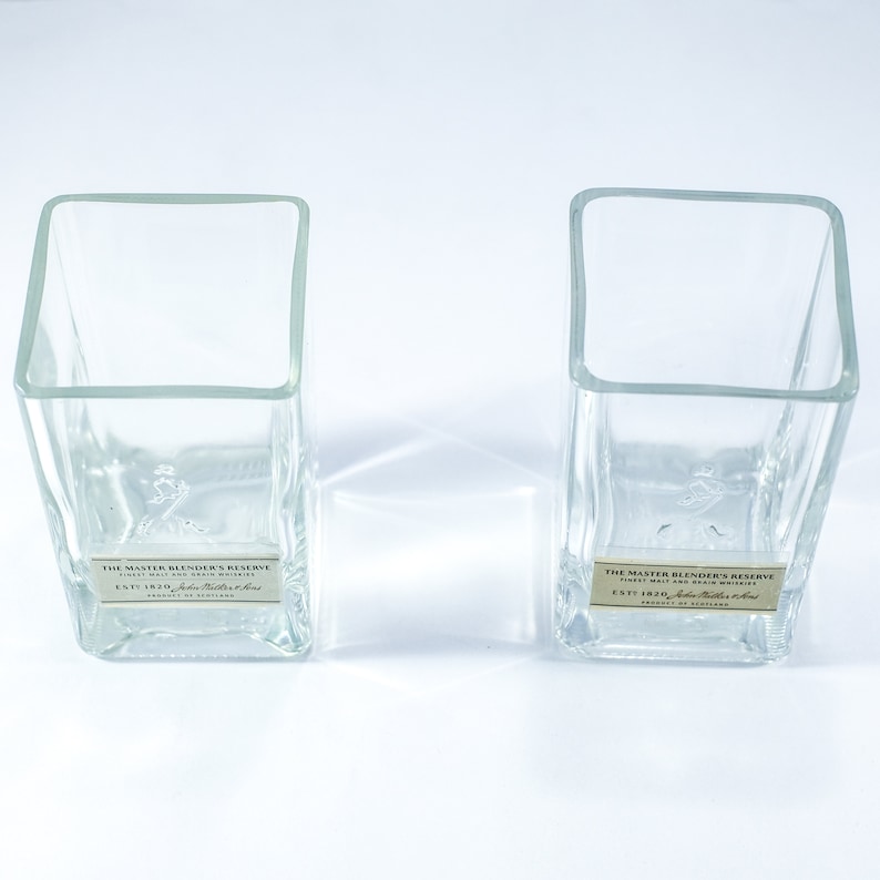 May include: Two clear glass tumblers with square bases. The tumblers are empty and have a label on the bottom that reads "The Master Blender's Reserve, Finest Malt and Grain Whiskies, Est 1820, John Walker & Sons, Product of Scotland."