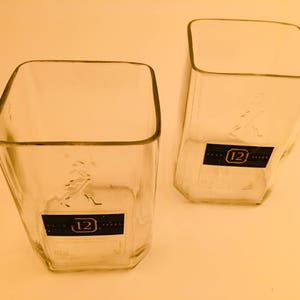 Op de afbeelding: Twee vierkante drinkglazen van helder glas met een 12 jaar oud whisky-etiket op de bodem.