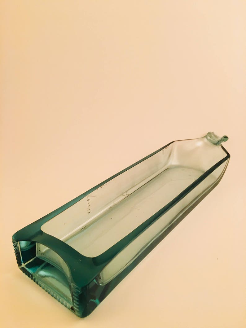 May include: A teal blue glass dish made from a recycled bottle. The dish is rectangular and has a smooth, polished surface.