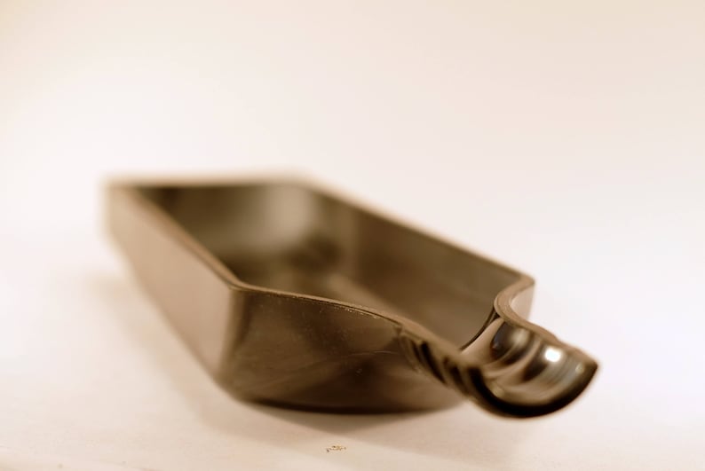 May include: A gray, plastic, elongated dish with a curved, rounded end. The dish is empty and appears to be made of a smooth, hard plastic.