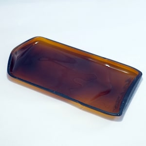 Puede incluir: Una bandeja rectangular de vidrio marrón con un borde marrón oscuro. La bandeja está hecha de vidrio reciclado.