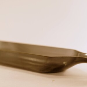 May include: A dark gray glass serving tray shaped like a bottle. The tray has a wide, flat base and a narrow, curved spout.