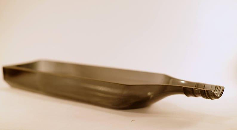 May include: A dark gray glass serving tray shaped like a bottle. The tray has a wide, flat base and a narrow, curved spout.
