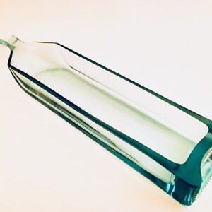 May include: A clear glass rectangular dish with a teal blue rim. The dish is empty and has a slight curve to it.