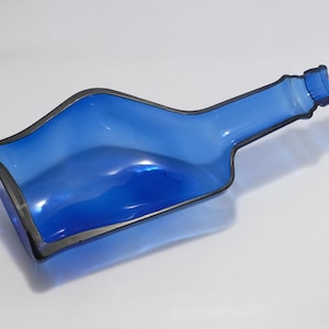 May include: A blue glass bottle with a unique, wavy design. The bottle is empty and has a broken top.