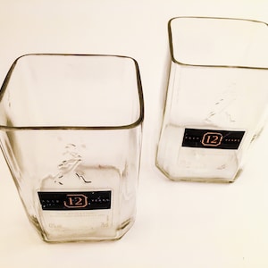Puede incluir: Dos vasos transparentes de vidrio con forma cuadrada. Los vasos están hechos de botellas de licor recicladas y tienen la etiqueta "12 años" en la parte inferior.