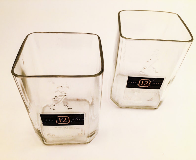 Op de afbeelding: Twee vierkante glazen van helder glas. De glazen zijn gemaakt van gerecyclede likeurflessen en hebben het label "12 jaar" op de bodem.