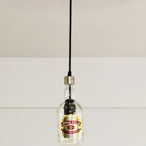 Peut inclure: Un luminaire suspendu en forme de bouteille en verre transparente avec une &eacute;tiquette dor&eacute;e indiquant "Chivas Regal 12" suspendu &agrave; un cordon noir.