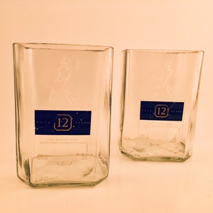 Op de afbeelding: Twee heldere glazen flessen met een blauw etiket waarop "Aged 12 Years" en "John Walker & Sons Established Kilmarnock 1820" staat.