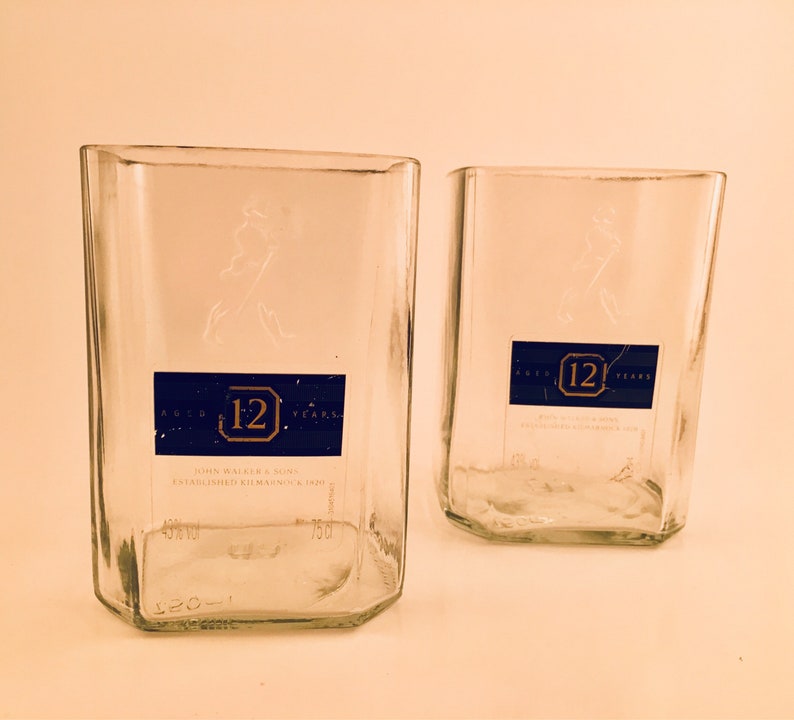 Op de afbeelding: Twee heldere glazen flessen met een blauw etiket waarop "Aged 12 Years" en "John Walker & Sons Established Kilmarnock 1820" staat.