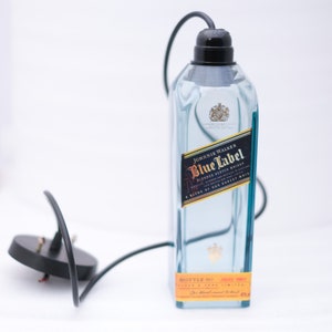 May include: A clear glass bottle with a black cord and plug. The bottle is labelled "Johnnie Walker Blue Label Blended Scotch Whisky A Blend of Our Rarest Whiskies". The bottle has a gold label with the text "Bottle No. 1443 1987", "Blended & Bottled", and "For blended Scotch whisky".