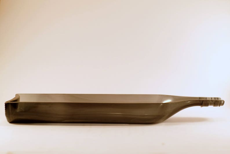 May include: A dark gray glass bottle with a long, narrow neck and a slightly curved base. The bottle is empty and has a smooth, polished surface.