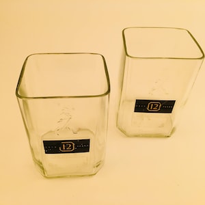 Op de afbeelding: Twee heldere glazen tumblers met een vierkante vorm en een 12-jarig whisky-etiket op de bodem.