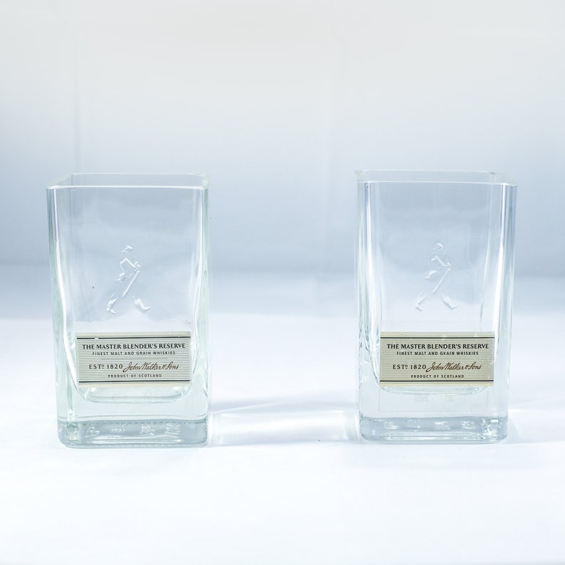 May include: Two clear glass tumblers with a walking man logo and the text "The Master Blender's Reserve Finest Malt and Grain Whiskies Est 1820 John Walker & Sons Product of Scotland" on the label.