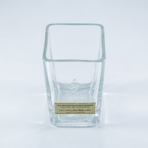 May include: A clear glass tumbler with a square base and a label that reads "The Master Blender's Reserve Finest Malt and Grain Whiskies Est 1820 John  Miller & Sons Product of Scotland".