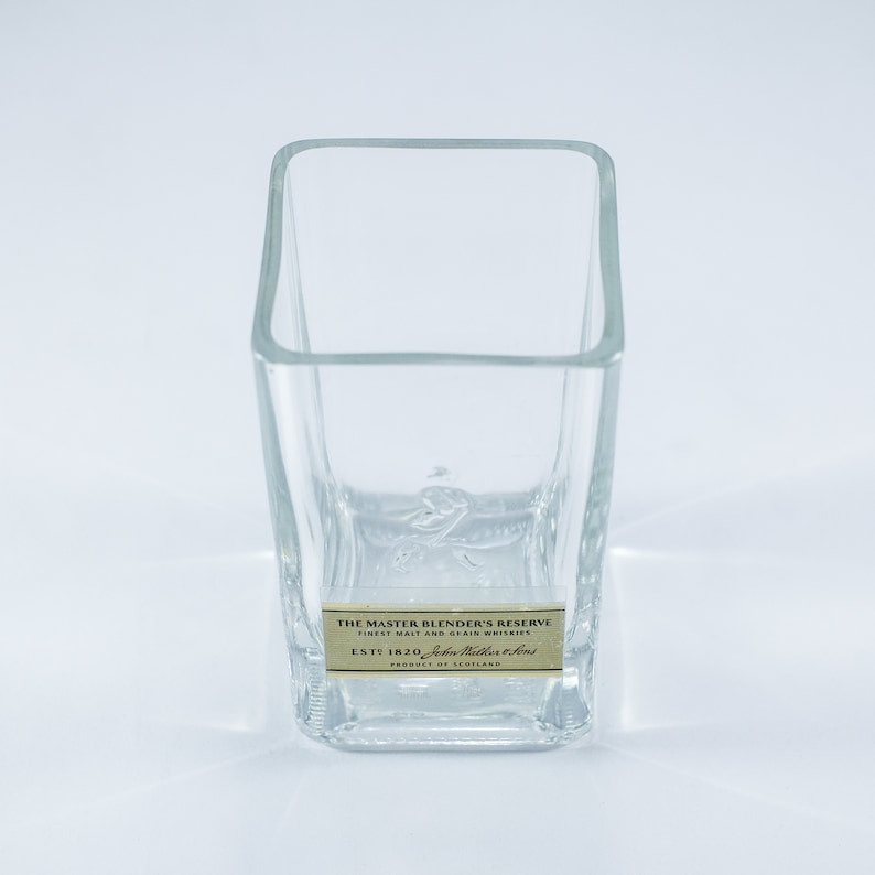 May include: A clear glass tumbler with a square base and a label that reads "The Master Blender's Reserve Finest Malt and Grain Whiskies Est 1820 John  Miller & Sons Product of Scotland".