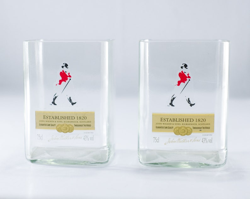 May include: Two clear glass tumblers with a gold label that reads "Established 1820 John Walker & Sons, Kilmarnock, Scotland" and a black and red silhouette of a man walking with a cane. The label also includes the text "Guaranteed  Last Quality" and "Throughout The World".