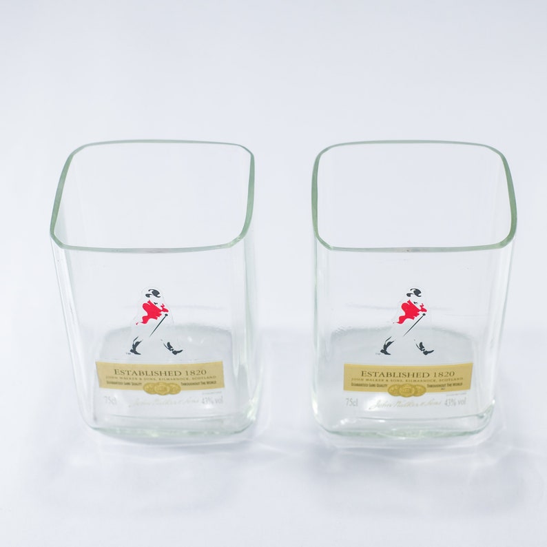 May include: Two clear glass tumblers with a square shape. Each glass has a label that reads "Established 1820" and features a black and white illustration of a man in a red jacket walking with a cane.